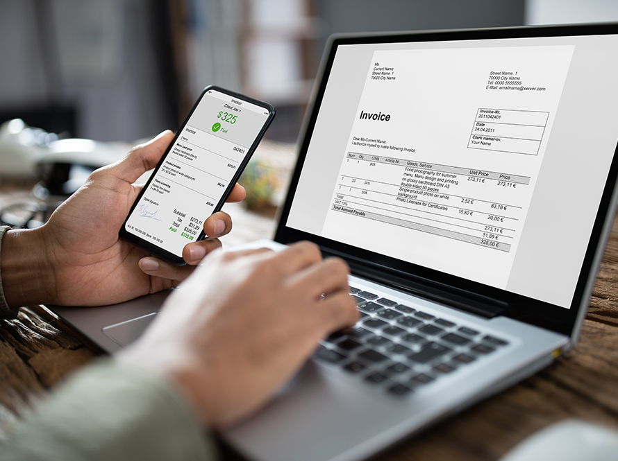 Someone sending an invoice on their laptop and holding a phone showing a client has paid them.