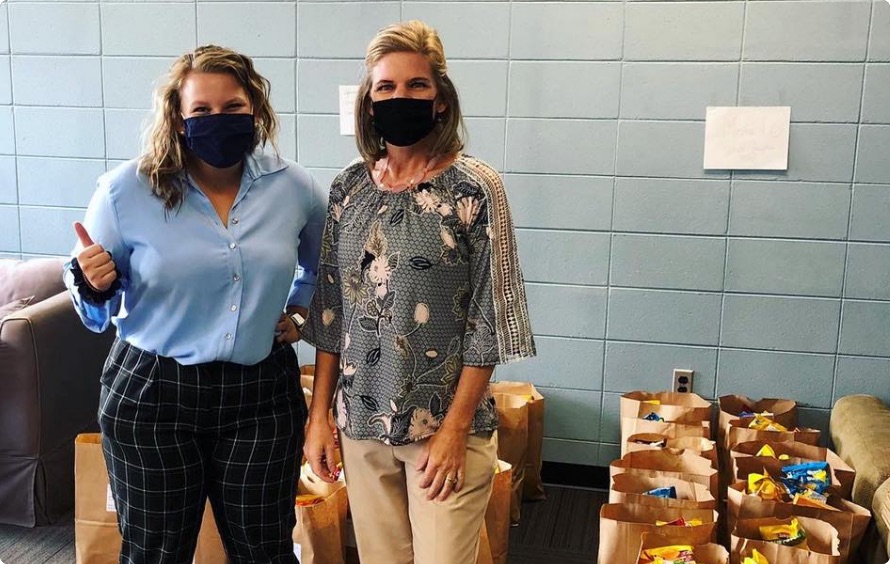 Two people wearing masks, one giving a thumbs up, in front of paper bags loaded with donations.
