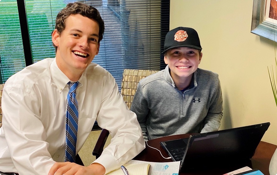 Two people smiling, one in business casual and the other in sports attire in front of a laptop.