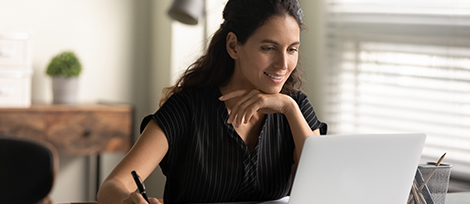 Woman looking at a laptop screen with a pen in her hand.