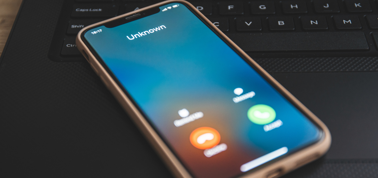 Phone laying on a laptop keyboard with an incoming call from an unknown caller.