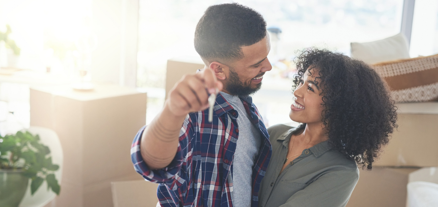 Happy couple holding house keys in front of moving boxes.