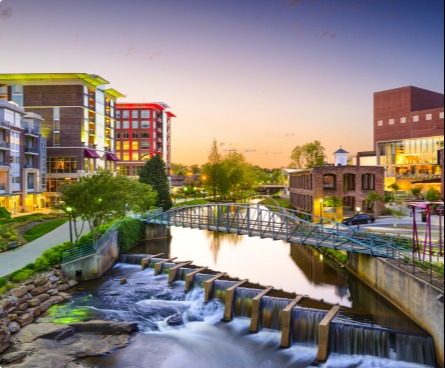 Greenville city view at sunset, with pedestrian bridge over a river and waterfalls.